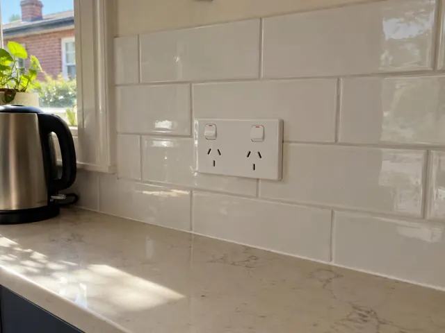 Double power point on glossy white tiled kitchen splashback above a stone bench in Clovelly