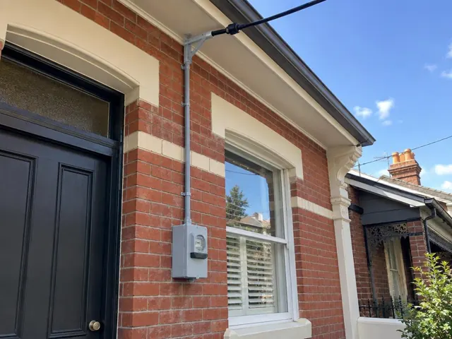 Overhead service cable and bracket on a brick house exterior with meter box in Waverley