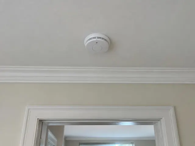 Ceiling-mounted smoke alarm above a doorway in a light painted hallway in Bronte