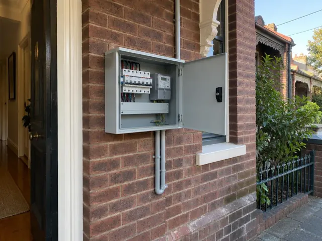 Open electrical switchboard on an exterior brick wall beside a doorway in a brick terrace house in Bondi